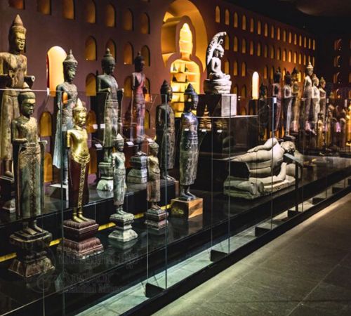 A row of ancient standing and reclining Buddha statues on display behind glass panels at the Angkor National Museum near Blanc Smith Hotel in Siem Reap.