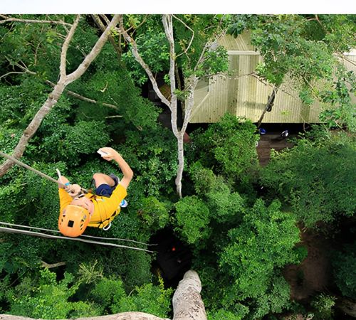 Overhead view of a person ziplining high above the lush rainforest canopy at Angkor Zipline in Siem Reap.