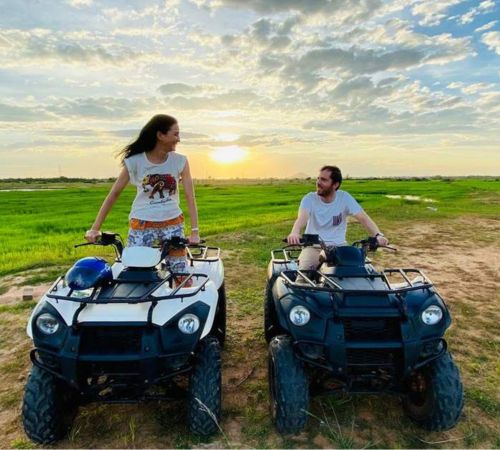A couple sitting on quad bikes looking out over the scenic green fields near Blanc Smith Hotel in Siem Reap.
