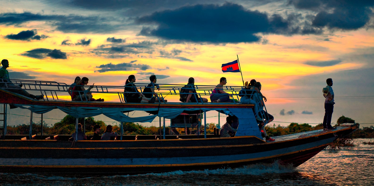 A group of tourists enjoying a sunset boat cruise with the Cambodian flag on Tonle Sap Lake near Blanc Smith Hotel in Siem Reap.
